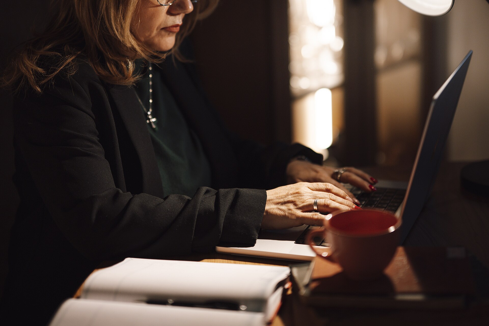 femme au bureau qui tape sur son ordinateur portable pour suivre ses devis, tasse de café et carnets sur la table